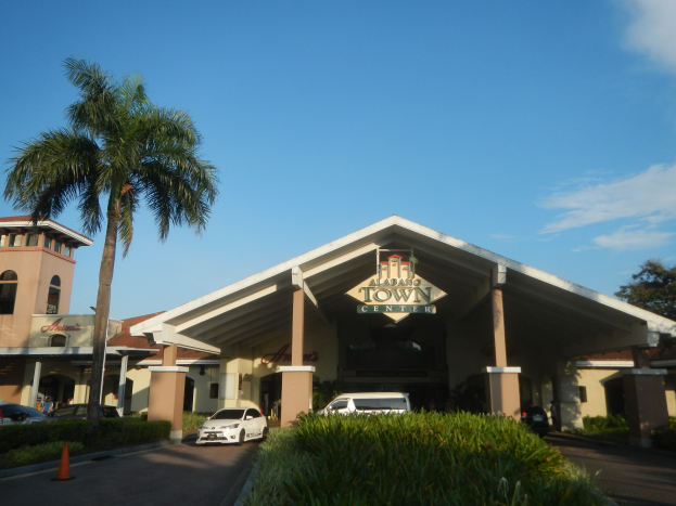 Der Eingang eines Resorts mit Palmen vorne, umgeben von Gebäuden, Fahrzeugen auf der Straße, Verkehrskegeln, Büschen, Bäumen und einem bewölkten Himmel im Hintergrund.