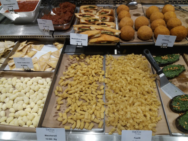 Ein Vitrine voller verschiedener italienischer Lebensmittel, darunter Schalen und Schüsseln mit verschiedenen Pastasorten, mit Schildern, die die Lebensmittelarten angeben.
