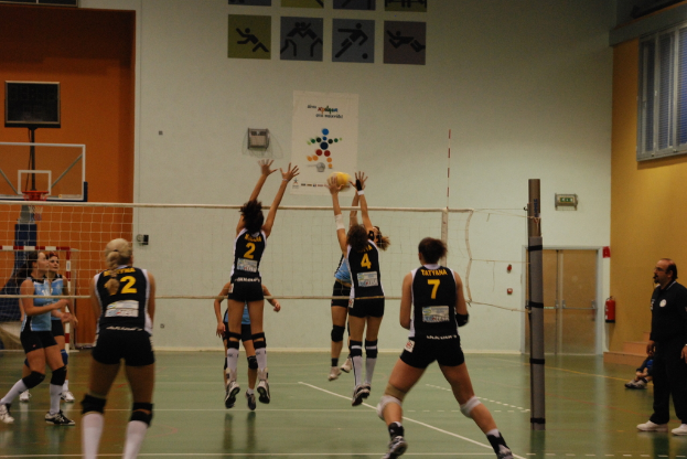 Ein Volleyballfeld mit aktiv spielenden Spielern, mit einem Basketballkorb, Fenstern und einer Tür im Hintergrund.