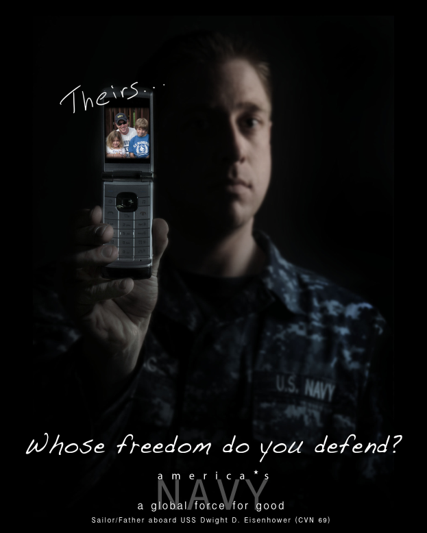 Ein Mann in einer marineblauen Uniform hält ein Handy hoch, auf dem der Text 'Wessen Freiheit verteidigst du?' zu sehen ist.