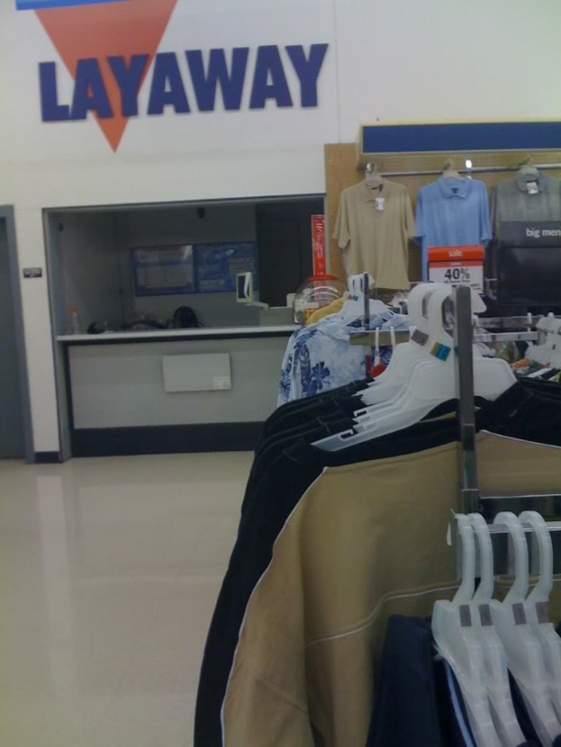 Ein Innenblick in einen Laden mit Kleidung an Bügeln, einem Tisch und einer Preistafel.