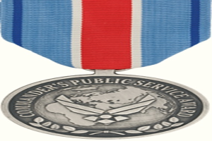 Eine silberne Medaille mit einer roten, weißen und blauen Schleife, auf der der Text 'Commander's Public Service Award' gegen einen weißen Hintergrund zu sehen ist.