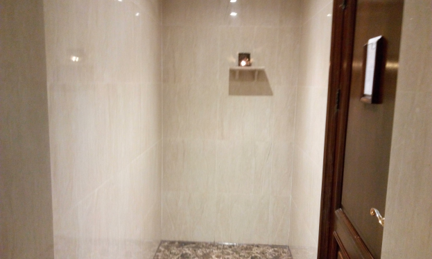 Ein Badezimmer mit einer Duschkabine neben einer Toilette, mit einer Tür auf der rechten Seite; geflieste Wände und Deckenleuchten schaffen eine warme Atmosphäre.