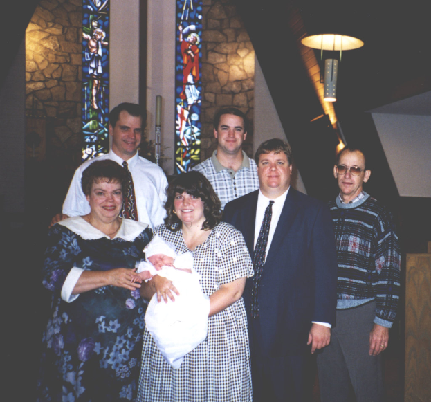 Eine Frau mit einem Baby auf dem Arm, vor einem hellen Hintergrund.