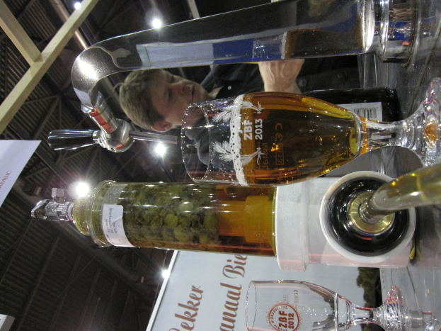 Eine Person steht vor einem Tisch mit Flaschen und Gläsern, die ein Getränk enthalten, einer Lampe auf dem Dach und einer Tafel mit Text davor.