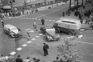 Schwarz-weiß-Szene eines Autounfalls an einer Straßenkreuzung mit mehreren Fahrzeugen, darunter ein Van, und einer Gruppe von Menschen, die herumstehen.