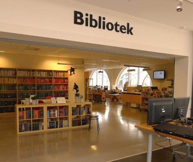 Mehrere hölzerne Regale mit Büchern, mit Monitoren auf der rechten Seite und dem Wort 'BIBLIOTECA' oben angezeigt.