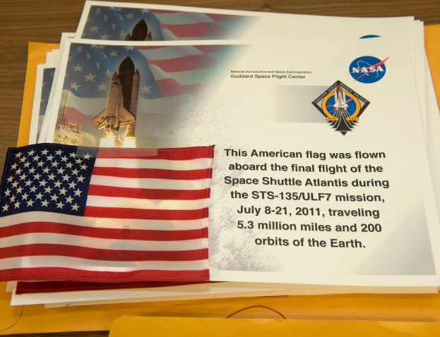 Poster mit Text, einer Flagge, einem Raketen und Logos sind in der Mitte zu sehen, mit einem Tisch unten und einem Boden oben im Bild.