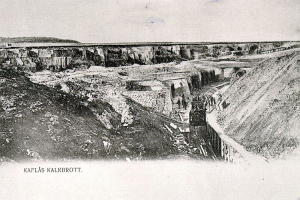 Ein altes Schwarz-Weiß-Foto eines Zuges, der in einen Tunnel einfährt, mit einer Brücke und Himmel im Hintergrund und Text unten, der "Kaflas Kalkbrott, das erste Bergwerk in Deutschland" lautet.