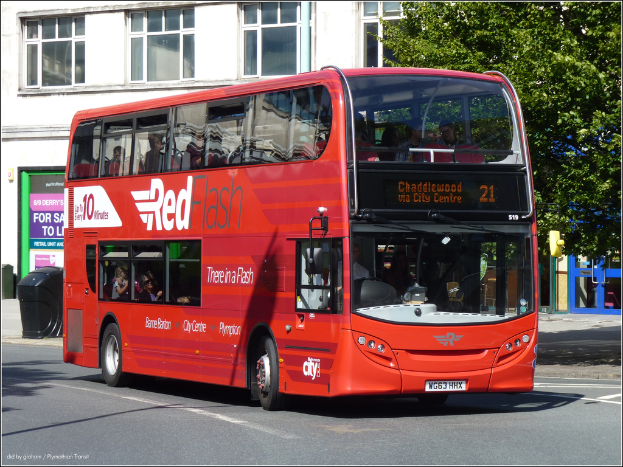 Ein roter Bus mit Text darauf ist in der Mitte, mit Menschen darin. Hinter dem Bus gibt es einen Baum und ein Gebäude mit einem Schild und einem schwarzen Müllcontainer davor. Rechts gibt es blaue und grüne Türen.