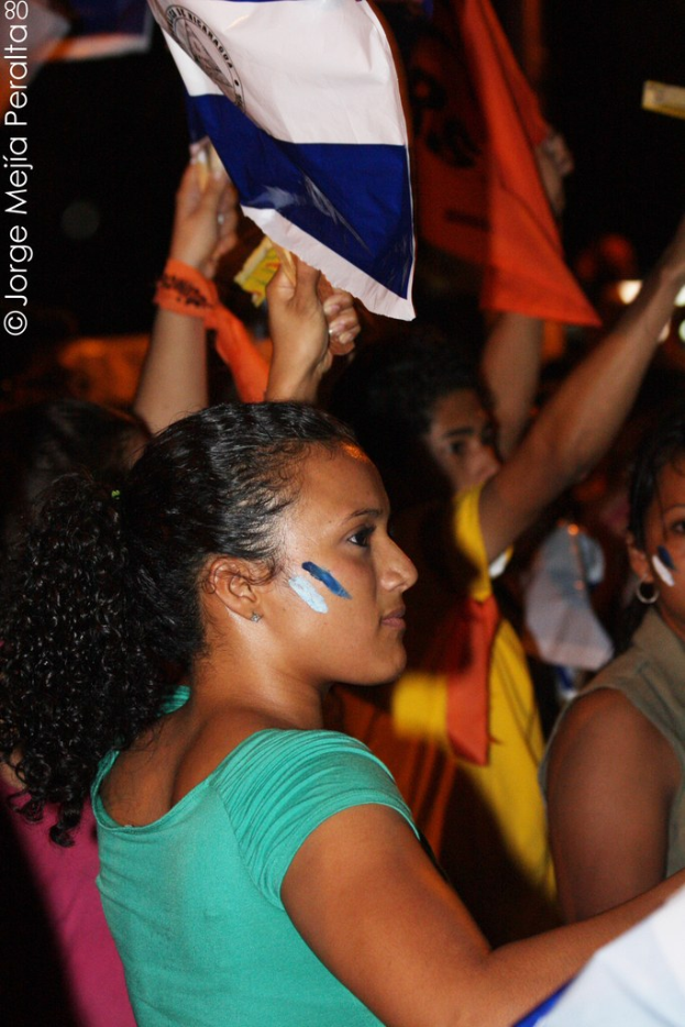 Frauen in grünen T-Shirts bei einer Demonstration, die weiße Stoffe halten, mit mehreren anderen Mädchen im Hintergrund.