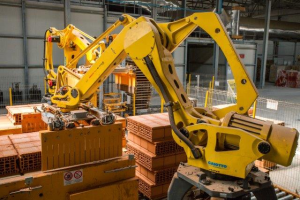 Ein großes Lager voller numerous Kisten, Kränen und diverser industrieller Ausrüstung, mit einem Zaun und Pfählen im Vordergrund und einer Wand im Hintergrund.